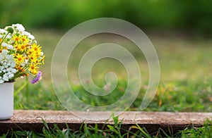 Beautiful wild flowers in white cup on wooden table and nature background