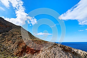 Beautiful wild red cliffs, clear blue sky, clouds. Diagonal view. Typical Greek landscape. Akrotiri peninsula, Chania