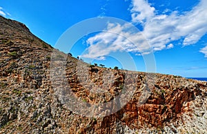 Beautiful wild red cliffs, clear blue sky, clouds. Diagonal view. Typical Greek landscape. Akrotiri peninsula, Chania