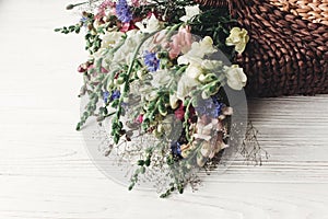 beautiful wildflowers in wicker bag on rustic white wooden background. colorful flowers in basket in light, space for text.