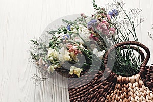 beautiful wildflowers in wicker bag on rustic white wooden background flat lay. colorful flowers in basket in light, space for te