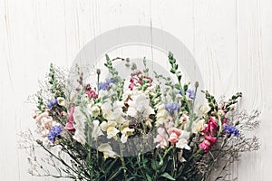 beautiful wildflowers in wicker bag on rustic white wooden background flat lay. colorful flowers in basket in light, space for te