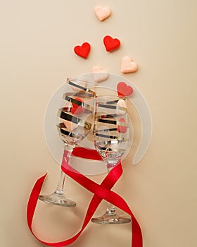 Beautiful wine glasses with candy-hearts on a beige background. Valentine`s day holiday. greeting card
