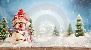 Beautiful winter background with  snowman on a wooden old desk, fir trees and blue sky. Winter, New Year and Christmas concept