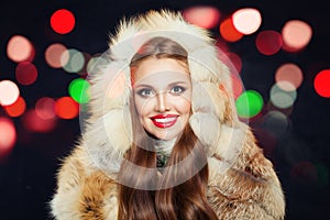 Beautiful winter girl with red nails in fur hood with colorful bokeh