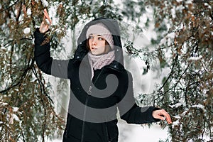 Beautiful winter girl stands in the park between the snowy trees