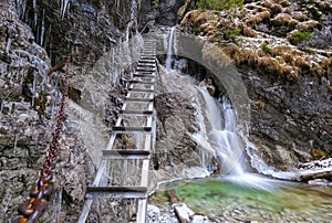 Beautiful winter hiking trail in gorge of Slovak Paradise NP. Metal climbing ladder with icefall and wild stream.