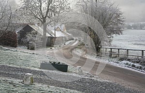 Beautiful Winter landscape of farm in fog in English countryside at dawn with hoarfrost covering trees and buildings