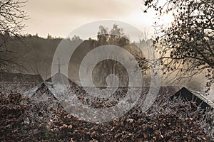 Beautiful Winter landscape of farm in fog in English countryside at dawn with hoarfrost covering trees and buildings