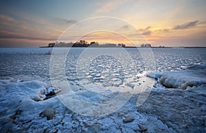 Beautiful winter landscape with frozen lake and sunset sky.