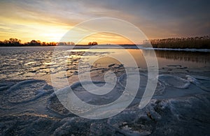 Beautiful Winter landscape with frozen river, reeds and sunset sky.