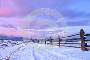 Beautiful winter landscape in the mountains. Sunrise with a colorful sky. Snowy road and wooden fence