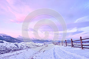 Beautiful winter landscape in the mountains. Sunrise. Snow covered road and wooden fence