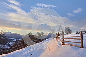 Beautiful winter landscape in the mountains. Sunrise. Snow covered road and wooden fence