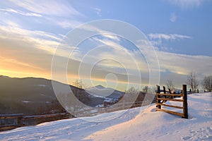 Beautiful winter landscape in the mountains. Sunrise. Snow covered road and wooden fence