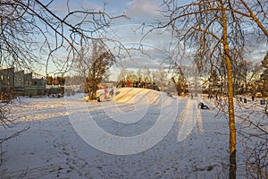 Beautiful winter landscape. Snow-covered hill where children go sledding and snowboarding with their parents in cottage village.