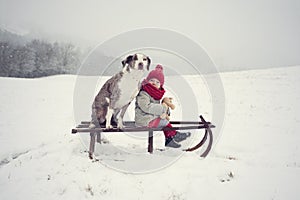 Beautiful winter. Little baby girl with her best friend dog sit on old wooden sledge in snow-covered landscape. Children