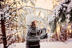 Beautiful winter portrait of child girl in sunny winter forest plays with snowy fir branch