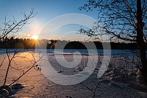 Beautiful winter scene. Sunset at the frozen lake covered with snow