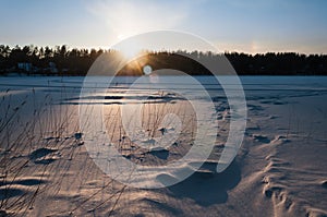 Beautiful winter scene. Sunset at the frozen lake covered with snow