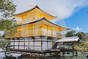 Beautiful winter seasonal of Golden Pavilion of Kinkakuji Temple with white snow falling and blue sky background at Kyoto.