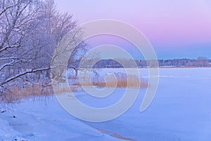 A beautiful winter sunrise scenery of frozen lake and forest. Colorful landscape with dawn skies