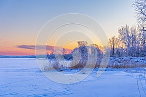 A beautiful winter sunrise scenery of frozen lake and forest. Colorful landscape with dawn skies