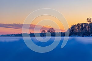 A beautiful winter sunrise scenery of frozen lake and forest. Colorful landscape with dawn skies