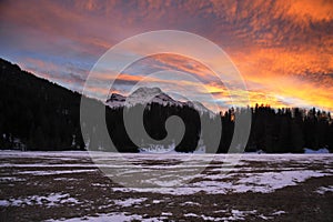 Beautiful winter sunset with orange cloud sky and snow Alps mountains and forest in Engadine region