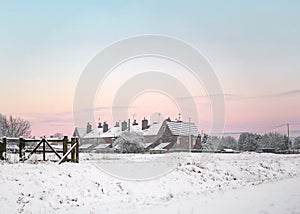 Beautiful winter sunset over row of old houses in countryside with deep snow and glowing sky. Snowy scene as sunrise at dawn pink.