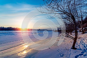 Beautiful winter sunset with trees in the snow and frozen river