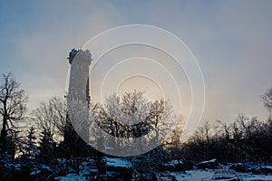 Beautiful winter view of frosted trees and rock at sunset, frozen lookout tower Sneznik