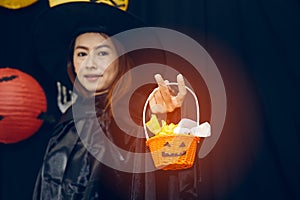 Beautiful Witch toss the candy in pumpkin basket on black background