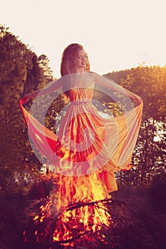 Beautiful witch in the woods near the fire. Magic woman celebrating Halloween. Girl doing witchcraft in the forest.