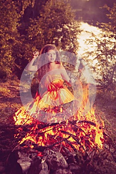 Beautiful witch in the woods near the fire. Magic woman celebrating Halloween. Girl doing witchcraft in the forest.