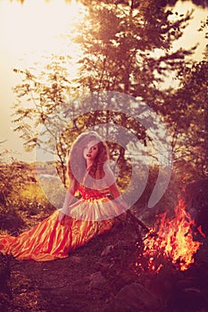 Beautiful witch in the woods near the fire. Magic woman celebrating Halloween. Girl doing witchcraft in the forest.