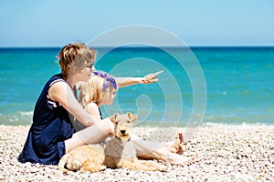 Beautiful woman with adorable daughter and dog sit on the beach