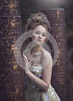 Beautiful woman in an ancient medieval dress, with a high complex historical hairstyle near the walls of the castle.