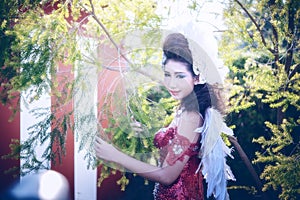 Beautiful woman with angle wings of red dress posing in garden