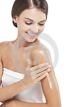 Beautiful woman applying body lotion to her arms while smiling