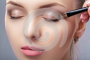 Beautiful woman applying brown eye shadow using makeup brush. makeup for blue eyes