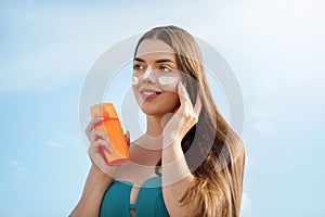 Beautiful woman applying cream sunscreen on tanned face. Sunscreen. Skin and body care.