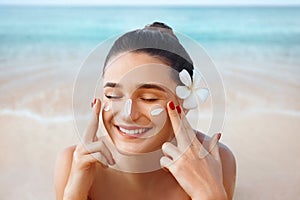 Beautiful woman applying cream sunscreen on a tanned face. Sunscreen. Skin and body care. The girl uses a sunscreen for her skin.