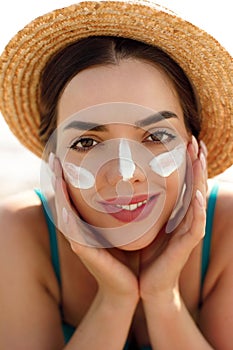 Beautiful woman applying cream sunscreen on a tanned face. Sunscreen. Skin and body care. The girl uses a sunscreen for her skin.