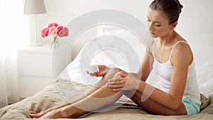 Beautiful woman applying cream to her legs at home