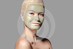 Beautiful Woman Applying Green Facial Mask. Beauty Treatments. Spa Girl Apply Clay Facial mask on grey background