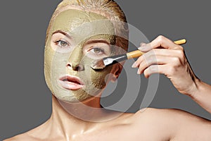 Beautiful Woman Applying Green Facial Mask. Beauty Treatments. Spa Girl Apply Clay Facial mask on grey background