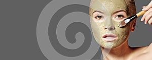 Beautiful Woman Applying Green Facial Mask. Beauty Treatments. Spa Girl Apply Clay Facial mask on grey background