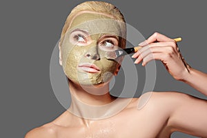 Beautiful Woman Applying Green Facial Mask. Beauty Treatments. Spa Girl Apply Clay Facial mask on grey background
