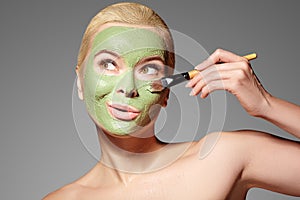 Beautiful Woman Applying Green Facial Mask. Beauty Treatments. Spa Girl Apply Clay Facial mask on grey background